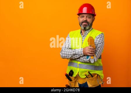 Middle-aged bearded man builder in uniform and hardhat with tools against orange background Stock Photo