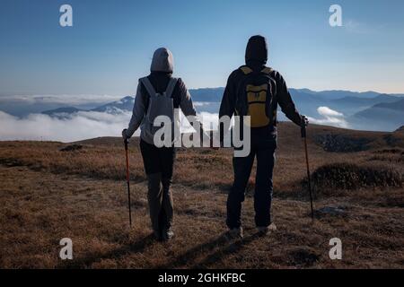 Hiking adventure healthy outdoors people standing talking. Couple enjoying view above clouds on trek. young woman and man in nature wearing hiking bac Stock Photo