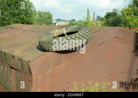 Tire from the wheel on the roof of a rusty garage. Used rubber for the car. Abandoned junk on the street. Old rusty garage for transport. Stock Photo