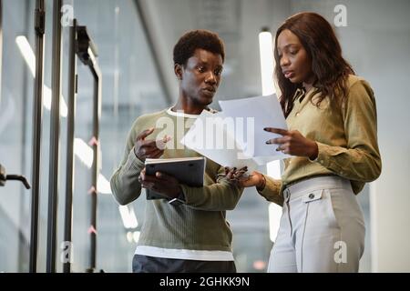 Serious business colleagues standing in office corridor and discussing sales report they prepares for meeting Stock Photo
