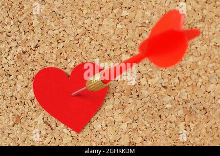 Dart arrow hitting in a red heart on pinboard - Concept of love Stock Photo