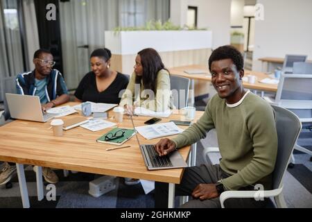 Portrait of smiling handsome young Black man attending business meeting and working on laptop Stock Photo