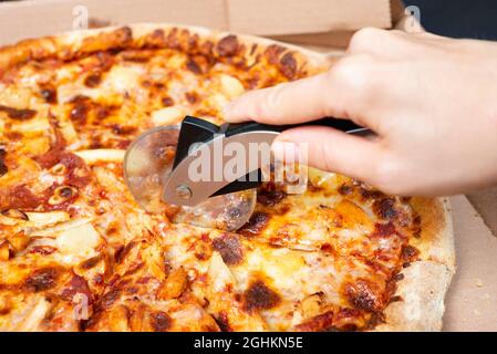 Close up on hand cutting pizza with pizza knife Tasty paperoni pizza in open box isolated on black background. Top view on paperoni pizza. Concept for Stock Photo