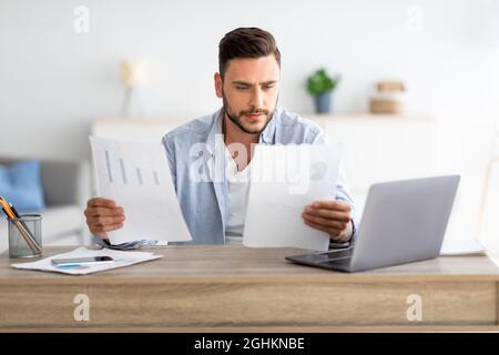 Millennial male self-entrepreneur working with papers at home office, checking annual financial reports, free space Stock Photo