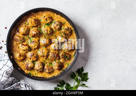 Swedish meatballs in creamy sauce in black frying pan, gray background, top view. Scandinavian food concept. Stock Photo
