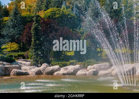 Big water fountain squirting water up in the air in Dikmen Valley Park in Ankara. Trees with different tones of green on the background. Stock Photo