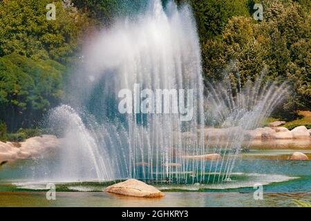 Big water fountain squirting water up in the air in Dikmen Valley Park in Ankara. Trees with different tones of green on the background. Stock Photo