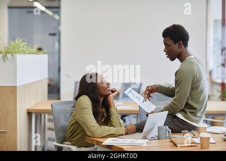 Happy young woman looking at colleague sitting on table and explaining his creative innovative business idea Stock Photo