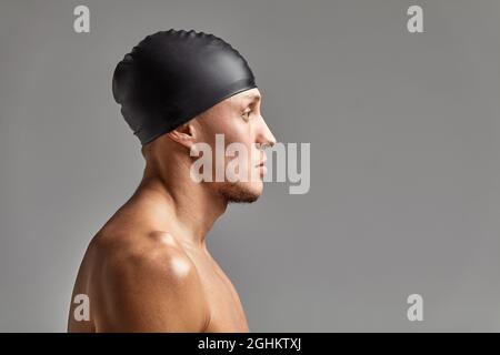 portrait of a young man swimmer wearing a rubber hat, standing against a gray background hat getting ready for training. Stock Photo