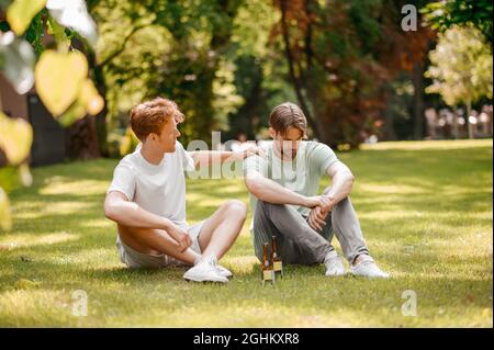 Two guys with bottles sitting on green lawn Stock Photo