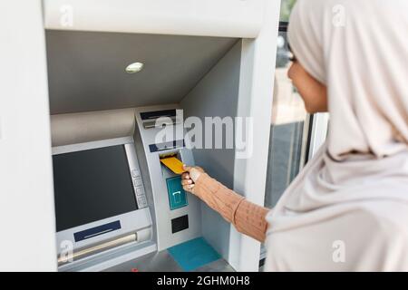 Currency, finance and transactions. Lady inserting an bank credit card into ATM machine to transfer money outdoor Stock Photo