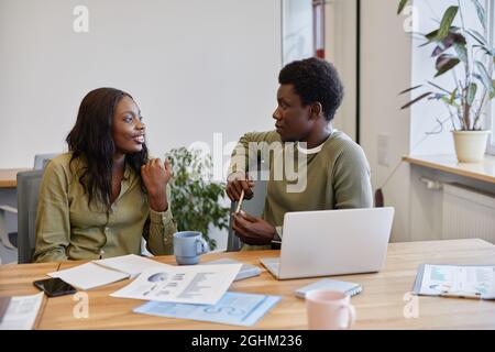 Young businessman listening to smiling coworker talking about her successful business project Stock Photo