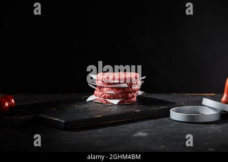 Stacked freshly made beef burger patties with patty former on a large black wooden cutting board in dim light with copyspace as a food template Stock Photo