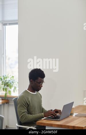 Frowning serious young businessman working on laptop at office desk and answering e-mails of customer or business partner Stock Photo