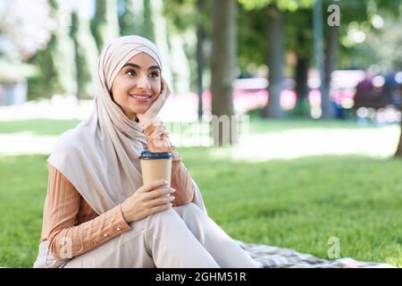 Smiling millennial arabian muslim woman student in hijab take a break from work or study, relax in park Stock Photo