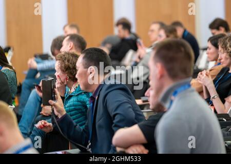 Side view of attentive serious businessman recording video of business lecture on mobile phone while participating in event with partners in modern co Stock Photo