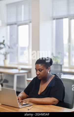 Portrait of serious female entrepreneur working on laptop at desk in modern office, filling forms online Stock Photo