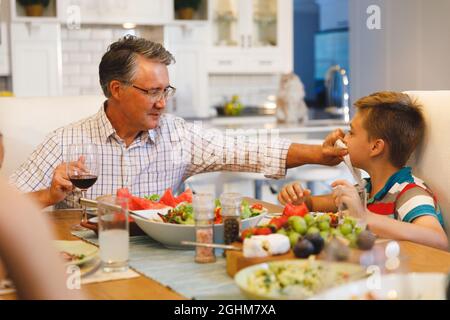 Caucasian grandfather wiping face of grandson while sitting at table and having dinner Stock Photo