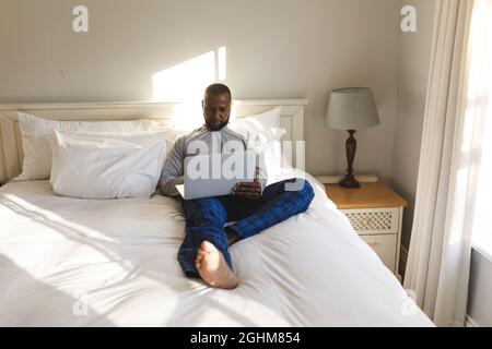 African american man using laptop and lying on bed in his bedroom Stock Photo