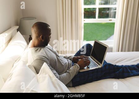 African american man using laptop and lying on bed in his bedroom Stock Photo