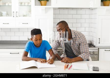 African american father and son in kitchen, doing homework together Stock Photo