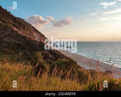 Beach Megali Petra sunset view. Greenery, hills and waves with pebble stones in sunset light. Coast of Lefkada island with steep cliffs in Greece. Sum Stock Photo