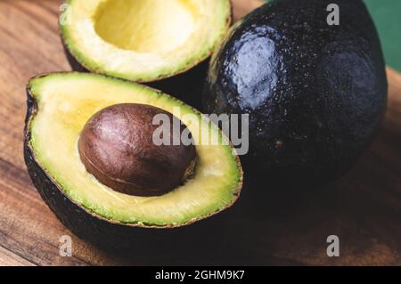 Halves of avocado Hass and whole avocado on wooden background. Stock Photo