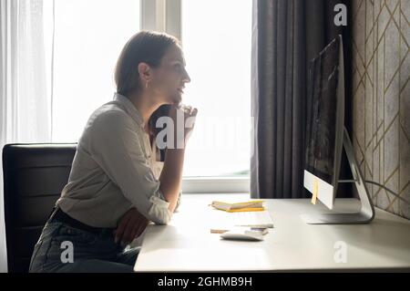 Concentrated woman staring at PC monitor, working remotely from home, focused female student researching topic, watching educational seminar or webinar, looks at computer screen sitting at desk home Stock Photo