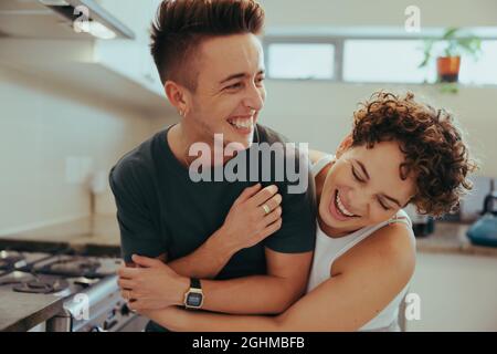 Young queer couple laughing together indoors. Happy young queer couple having fun together while standing in their kitchen. Romantic young LGBTQ+ coup Stock Photo