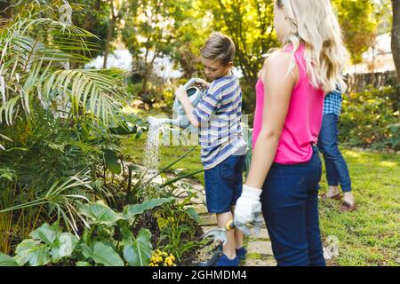 Caucasian son and daughter watering plants in garden with mother and father in background Stock Photo