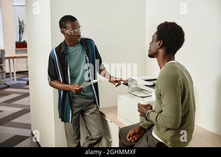 Coworkers standing near office printer, making copies of documents and discussing project development Stock Photo