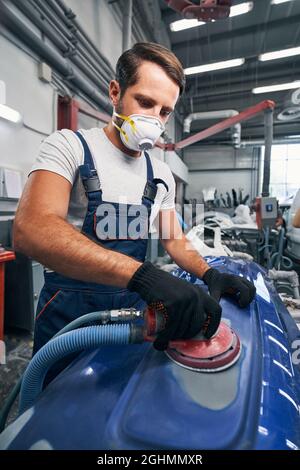 Auto mechanic in respirator using sander on car surface Stock Photo