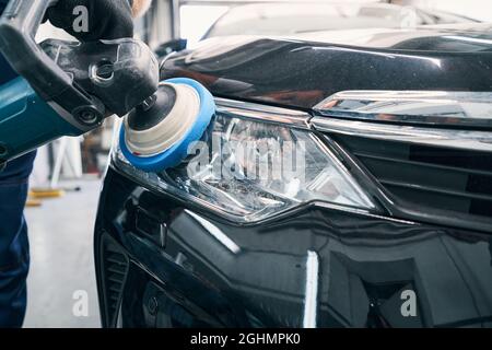 Repair workshop specialist cleaning headlight with polisher Stock Photo