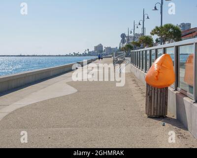 Long empty Piale Pasha concrete promenade along the mediterranean sea with airplane getting down to Larnaca airport. Orange plastic bin bag puffing. Stock Photo