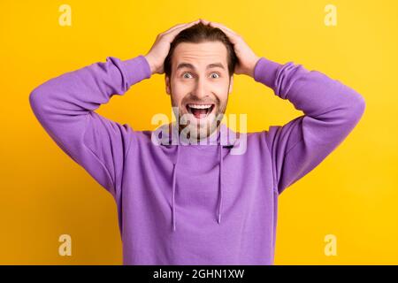 Photo of funky positive astonished guy hands head open mouth wear violet hoodie isolated yellow color background Stock Photo