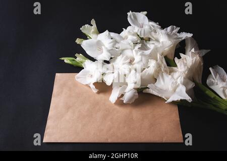 bouquet of white gladioli on black background with envelope in vintage style Stock Photo