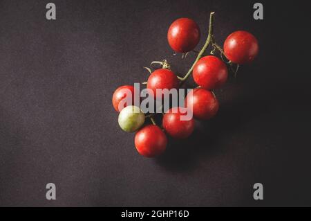 bunch of fresh cherry tomatoes on a branch are located on a black serving board on a dark background Stock Photo