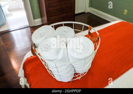 A basket of organized clean rolled white towels for guests sitting on a bed in a guest bedroom Stock Photo