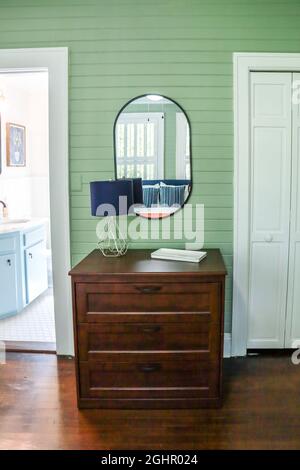 A simple dark wood stained dresser in a guest bedroom with green panel  shiplap walls and a black rimmed mirror and small lamp Stock Photo - Alamy