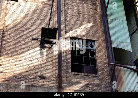 Face of a derelict brick industrial building, rusted metal exterior structures, broken windows and aged green fiberglass, horizontal aspect Stock Photo