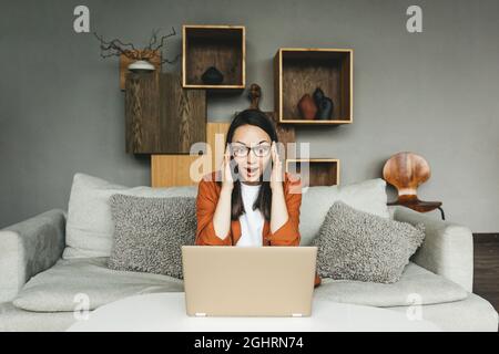 A very surprised young woman with glasses works from home.  Stock Photo