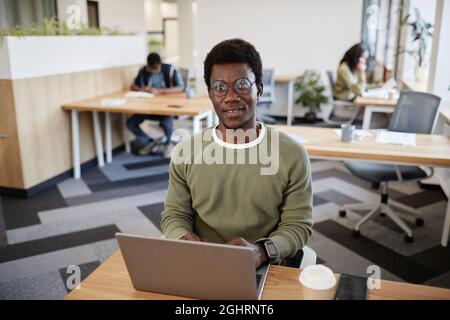 Portrait of smiling young businessman in glasses working on laptop at office desk and answering e-mails of customers and coworkers Stock Photo