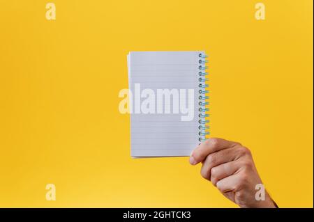 Male hand holding blank spiral notepad over yellow background. With copy space. Stock Photo