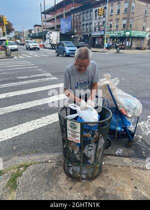 Chinese man going through a trash can to retrieve aluminum cans for collection on Fort Hamilton Parkway in Brooklyn, New York. Stock Photo