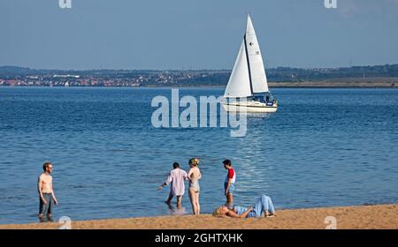 Portobello, Edinburgh, Scotland, UK weather. 7th September 2021. Sunny, hot afternoon at the seaside with temperature of 21 degrees. not over busy but people arriving late afternoon perhaps after work. Pictured: The 'Remedy' sailing boat in the background out on the Firth of Forth Stock Photo