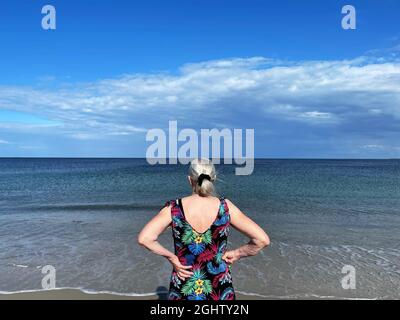 Rear view of a senior woman standing on beach looking out to sea, Samsoe, Jutland, Denmark Stock Photo