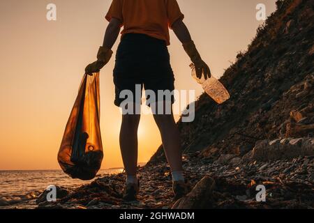 Zero waste. Silhouette of a volunteer holding a plastic bottle and posing on the beach. Sunset in the background. The concept of Earth Day and environ Stock Photo