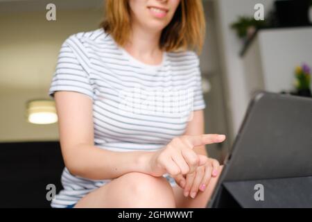Casual woman uses tablet for inline conversation. Freelancer working online at modern living room.  Stock Photo