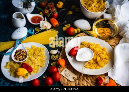 Raw pasta on a table with ingredients for making a tomato, chilli and garlic sauce with a glass of white wine Stock Photo