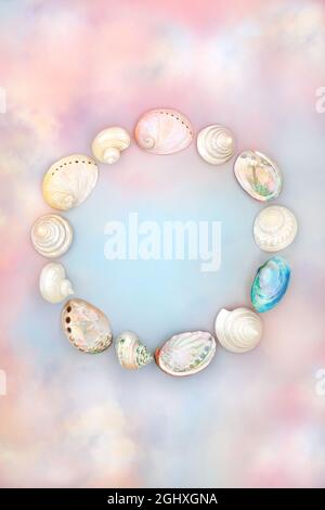 Sea shell abstract wreath with mother of pearl shells on rainbow coloured sky and cloud background. Creative nature arrangement. Flat lay, top view. Stock Photo